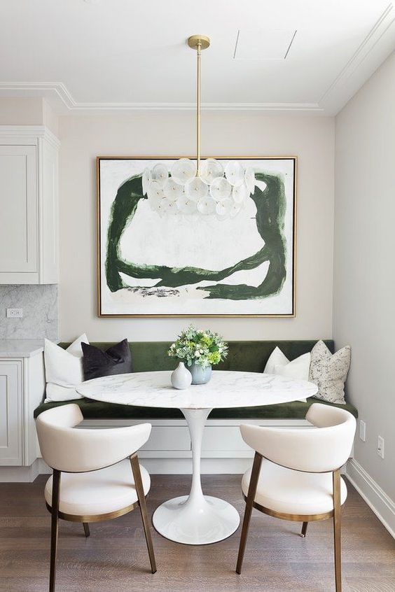 A lovely contemporary dining nook with a green built in bench, an oval table, creamy chairs, a refined chandelier and a green artwork