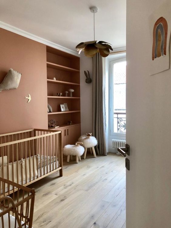 a lovely contemporary nursery in muted color, with a rust accent wall and built-in shelves, stained cribs, faux fur stools and grey curtains