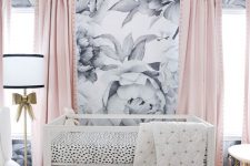 a lovely contemporary nursery with a floral print accent wall, pink curtains, an acrylic crib, gold touches and a white chair is cool