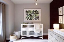 a modern monochromatic nursery with grey walls and a black accent wall, a white crib, a stained dresser and changing table, a striped rug and lovely prints on the walls