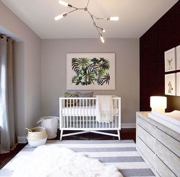 a modern monochromatic nursery with grey walls and a black accent wall, a white crib, a stained dresser and changing table, a striped rug and lovely prints on the walls