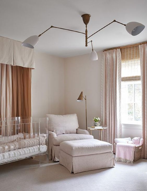 a pretty contemporary nursery in nrutrals, with an acrylic crib, a neutral chair and a footrest, a basket and neutral curtains