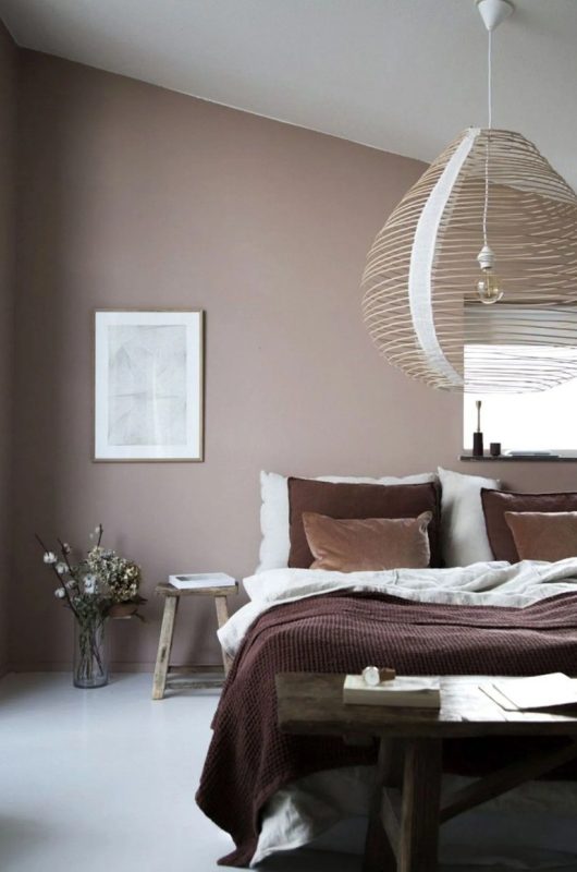 a relaxed bedroom with a taupe accent wall, a wooden bed and stools, an oversized wooden lampshade and some art