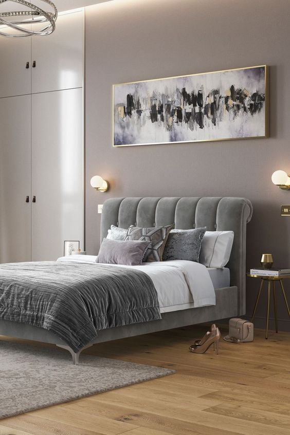 A sophisticated taupe bedroom with built in wardrobes, a grey upholstered bed with grey bedding, a statement artwork and some lights