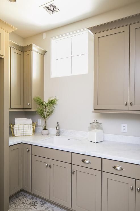 a stylish small taupe kitchen with vintage shaker cabinets, a white stone countertop, a small window and neutral knobs is a chic space