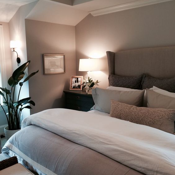 a taupe bedroom with taupe walls, an upholstered bed, dark stained nightstands and lots of lamps plus a statement potted plant