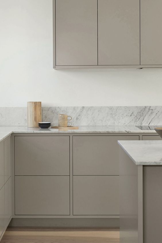 a very minimal kitchen with sleek taupe cabinets, white stone countertops and a backsplash plus gold touches is a stylish solution to rock