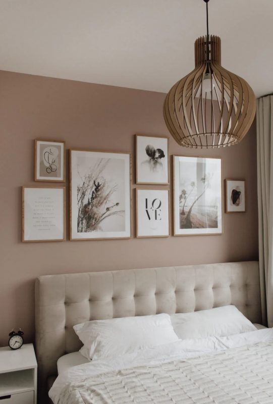 a welcoming bedroom with taupe walls, an upholstered neutral bed, white nightstands, a plywood lamp and a chic gallery wall