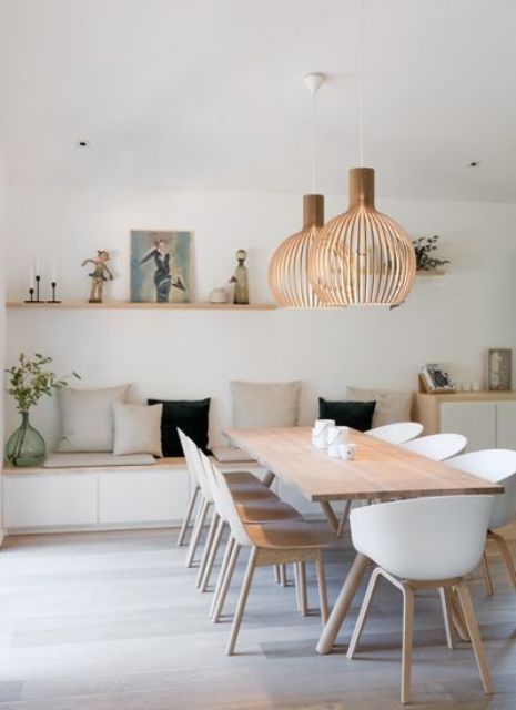 An airy contemporary dining room with a built in storage bench, pillows, a light stained table and white chairs, pendant plywood lamps