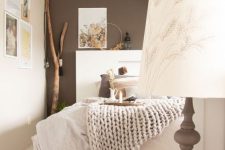 an eye-catchy boho bedroom with a taupe accent wall, a gallery wall, a white bed and neutral bedding, an artwork and a woven lamp