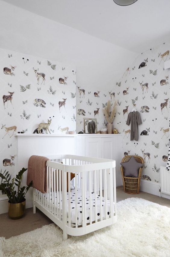 An eye catchy contemporary nursery with flora and fauna wallpaper, a white crib and paneling, a little peacock chair and a fluffy rug