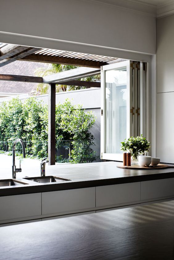 A folding window opens the kitchen to outdoors, and turns it into an outdoor indoor space easily and with style