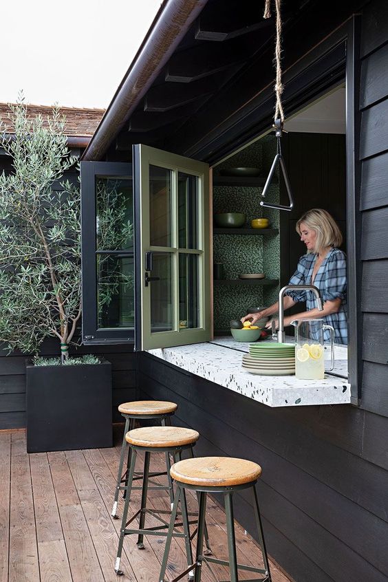 a black outdoor space with tall stools, a folding pass through window, a terrazzo windowsill that doubles as a table