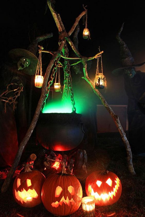 a fab Halloween outdoor decoration of a cauldron with green smoke, candle lanterns, jack-o-lanterns under it is a lovely idea