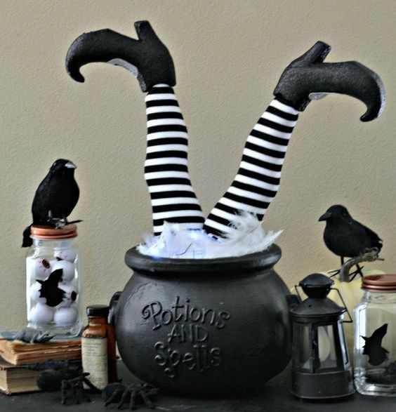 a Halloween decoration of a cauldron with witch's legs, candle lanterns, blackbirds and vintage books is amazing