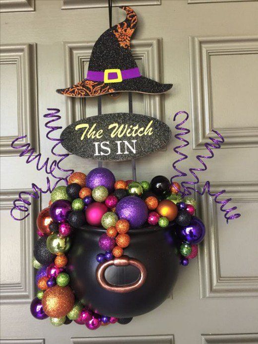 a Halloween door decoration of a witches' cauldron with colorful glitter Christmas ornaments, a witch hat and some curls is a cool idea