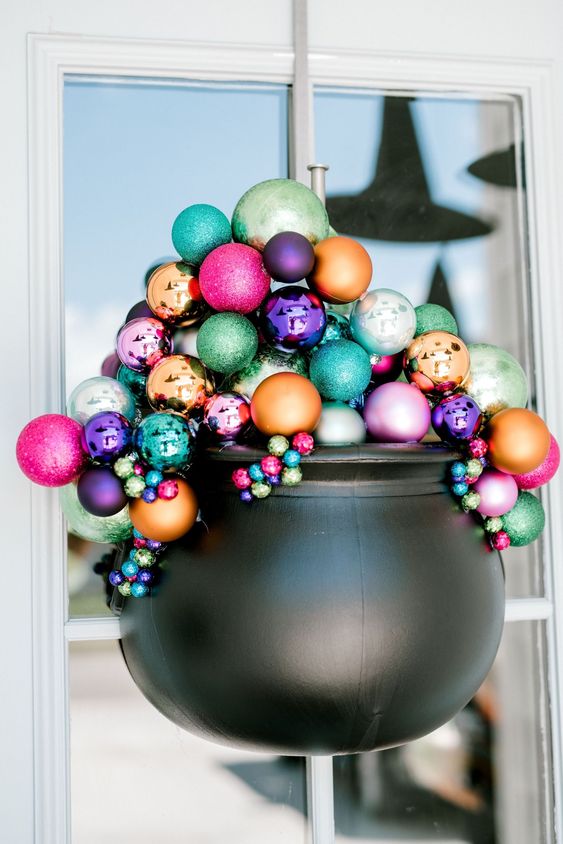 a lovely front door decoration of a cauldron filled with colorful Christmas ornaments is a gorgeous alternative to a usual Halloween wreath