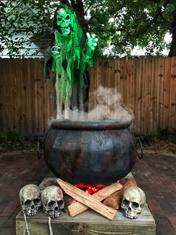 an outdoor Halloween decoration of a realistic cauldron, firewood and lights, skulls and some smoke is amazing