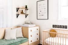 a Nordic chic nursery with white and stained furniture, a built-in sofa, a brigth striped rug, open shelves and a printed pouf