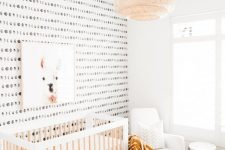 a boho Scandi nursery with lunar wallpaper, a neutral crib, a rocker, a coffee table and a jute pouf plus a pendant lamp