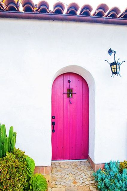 a bright pink arched wooden door with a small window and a black handle is a fantastic solution for a mansion or a French or Spanish country house