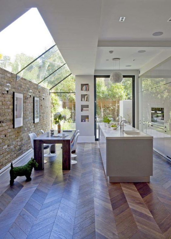 a chic contemporary space with a sleek white kitchen and a dining space lit up with a large window that flows into a large skylight