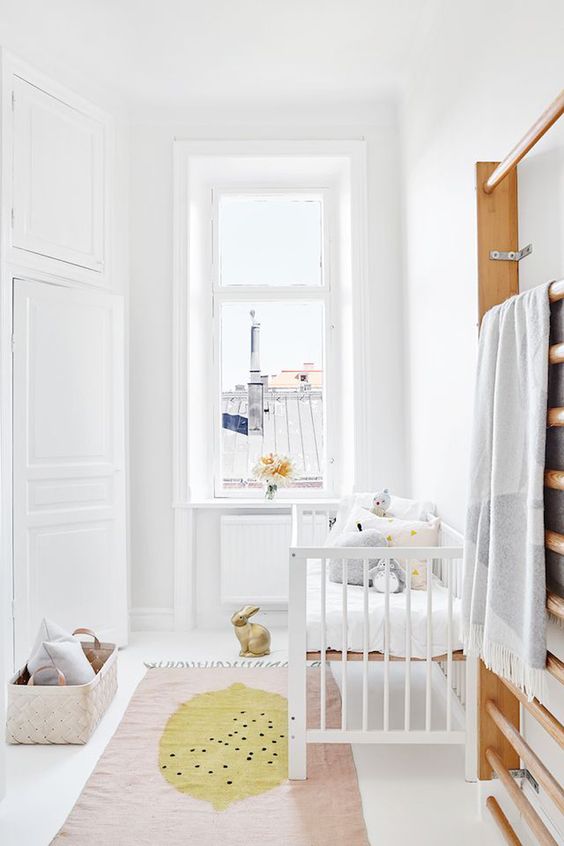a chic neutral Scandi nursery with white furniture, pastel pillows and a rug, a basket for storage is a small and cute space