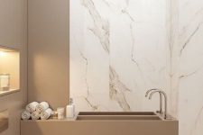 a contemporary and refined bathroom clad with white marble tiles, with a greige wall and a built-in sink plus built-in lights is cool