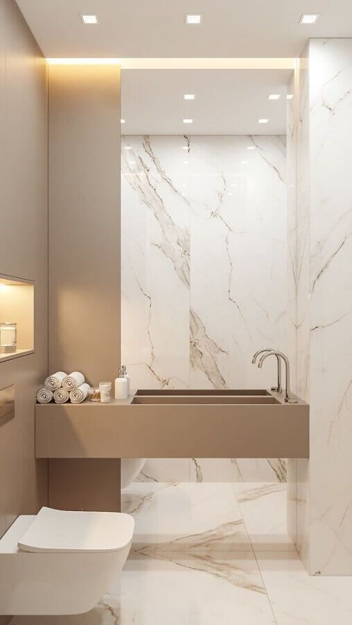 A contemporary and refined bathroom clad with white marble tiles, with a greige wall and a built in sink plus built in lights is cool