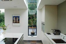 a contemporary and sleek kitchen with a narrow window that goes into a skylight, and they fill the space with natural light