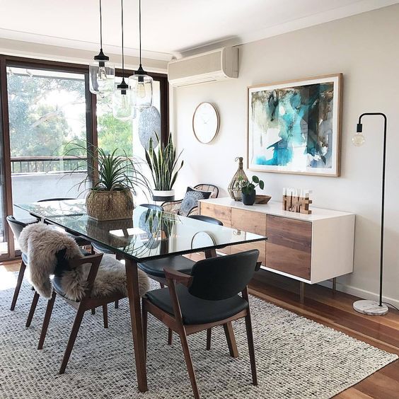 a cool modern greige dining room with a stylish credenza, a glass table and black chairs, pendant bulbs, potted plants and a floor lamp