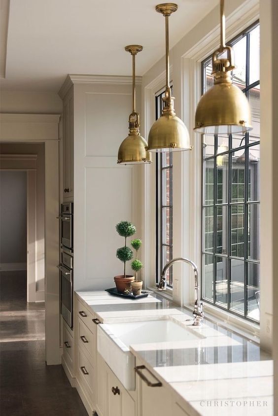 a cozy and welcoming neutral farmhouse kitchen with white stone countertops, French windows, brass pendant lamps