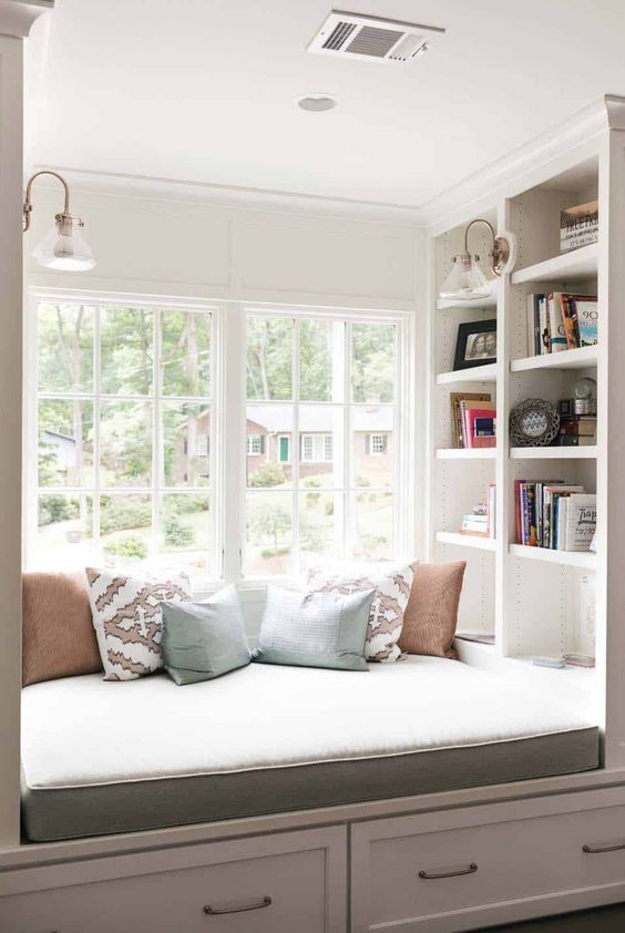 A cozy reading nook by the window   an upholstered bench with pillows and some shelves built in here and there