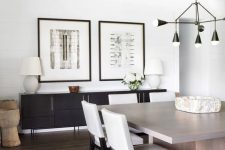 a farmhouse dining room with reclaimed wooden beams, a black credenza, a greige dining table and white chairs plus a black chandelier