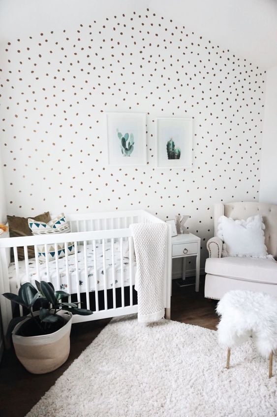 a fresh neutral nursery with a spotted accent wall, white and creamy furniture, a neutral rug and bedding, a mini gallery wall