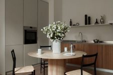 a greige kitchen combined with a kitchen, light-stained furniture, a round table and woven chairs, a grey storage unit, a long shelf and some blooms