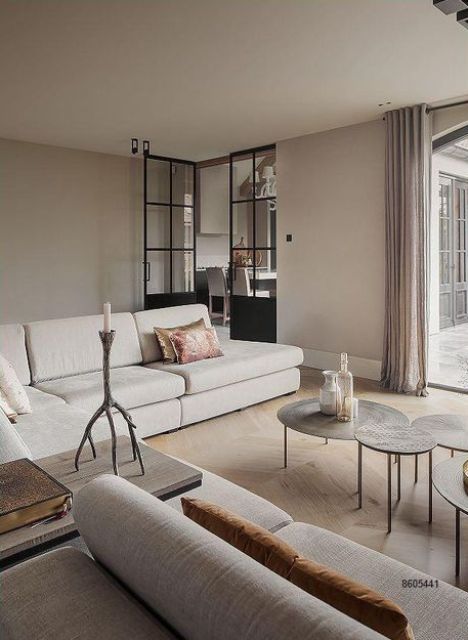 a greige living room with a large neutral sectional, round hammered coffee tables and mustard pillows is an ethereal and lovely space