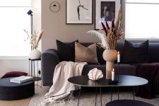 a greige living room with black seating furniture, a black coffee table, a mini gallery wall, black and tan pillows, a terracotta vase and some grasses