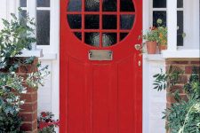a hot red front door with glass panes and refined metal touches, with greenery and bold red blooms that echo with the door