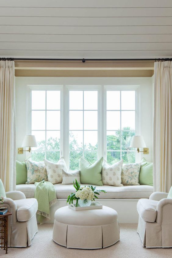 a large French window with a cozy windowsill sofa styled with lots of pillows that is a lovely alternative to a usual sofa in the living room