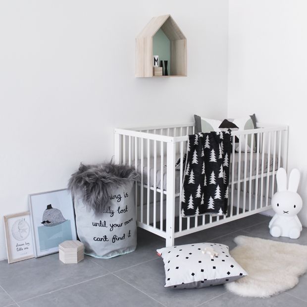 a modern Nordic nursery with a white crib, mmonochromatic bedding, some artworks, a basket for storage and toys of course