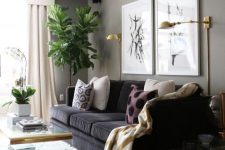 a lovely greige living room with a black sofa, a mini gallery wall, gold sconces, acrylic side tables and a coffee table plus statement plants