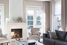 a lovely greige living room with greige textiles, a fireplace, graphite grey sofas, a wooden coffee table and elegant creamy chairs