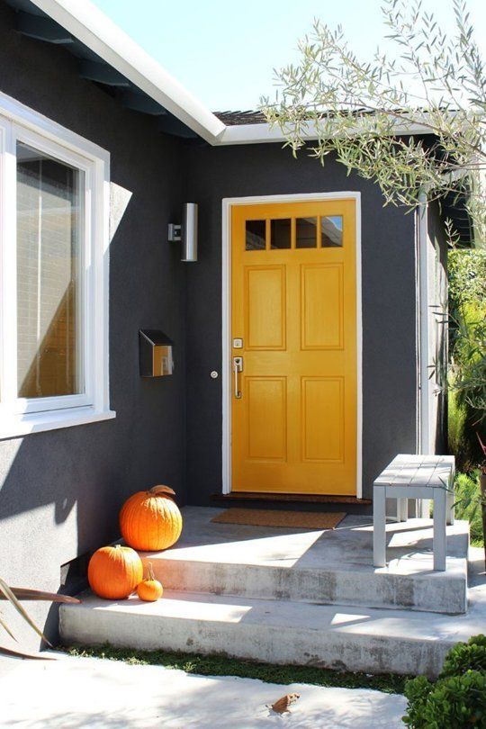 a marigold door with glass panes makes a bold statement with graphite grey walls around and orange pumpkins on the steps is a cool modern solution