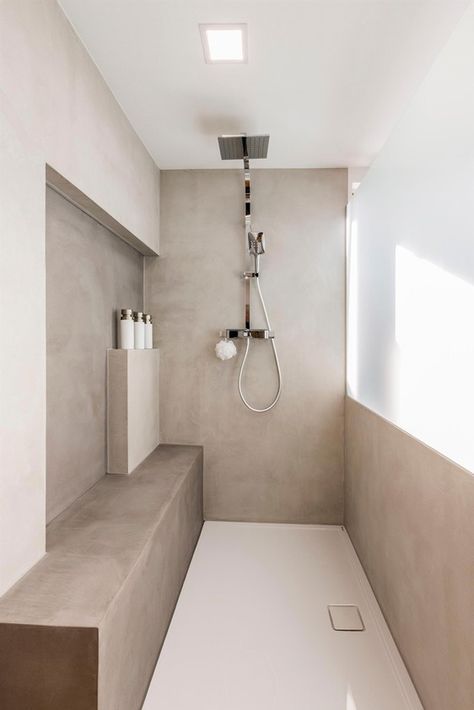 a minimalist greige bathroom with a concrete shower space, a window, some shelves for storage and a built-in bench for seating