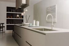 a minimalist greige kitchen with a sleek oversized kitchen island, a hood and hanging lamps plus built-in niches for tableware