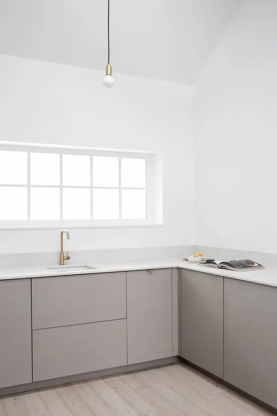 a minimalist greige kitchen with sleek cabinets, white stone countertops, brass touches and white walls is amazing