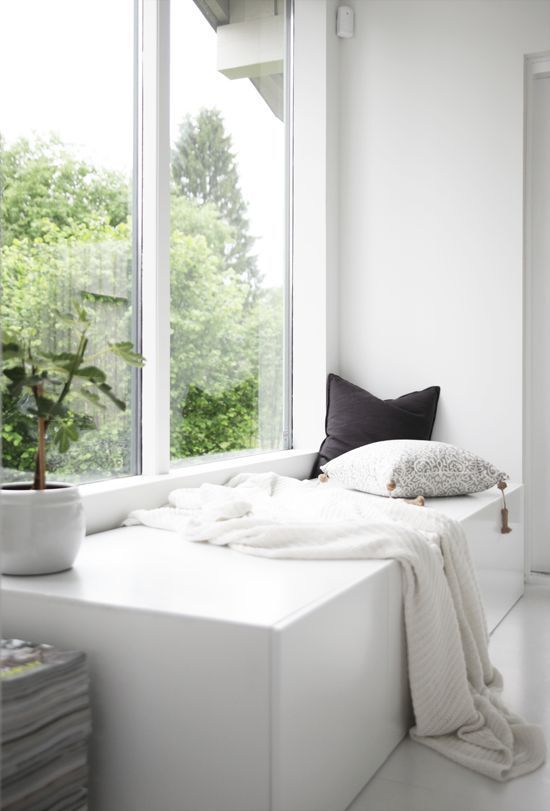 a minimalist space with a double-height window and a storage daybed built-in, with pillows and a blanket is a cool and stylish idea