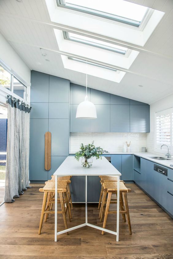 a modern blue kitchen and dining space are lit not only with windows but also with the help of skylights