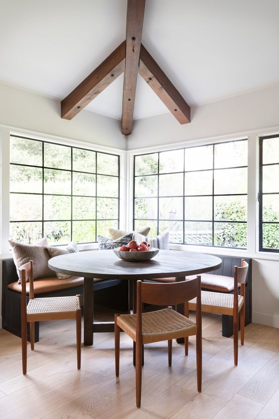 a modern farmhouse dining space with large French windows, a corner seating, a round table, woven chairs and neutral and printed pillows